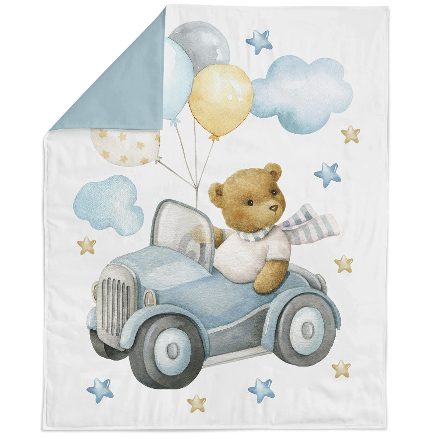 Baby blanket with teddy bear in a car, balloons, and clouds on a white background